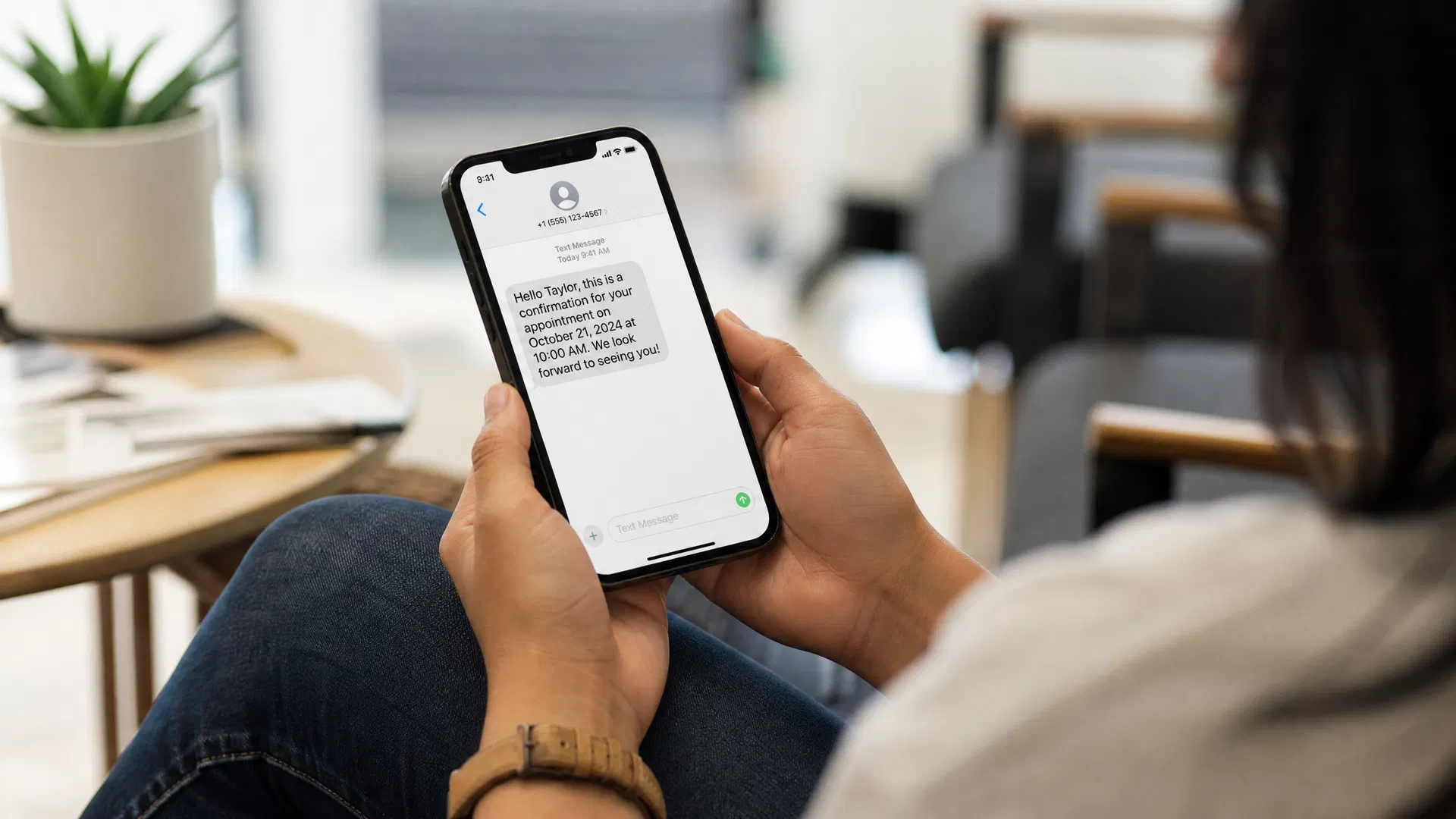 Person reading an appointment confirmation text message on a smartphone in a bright modern waiting area