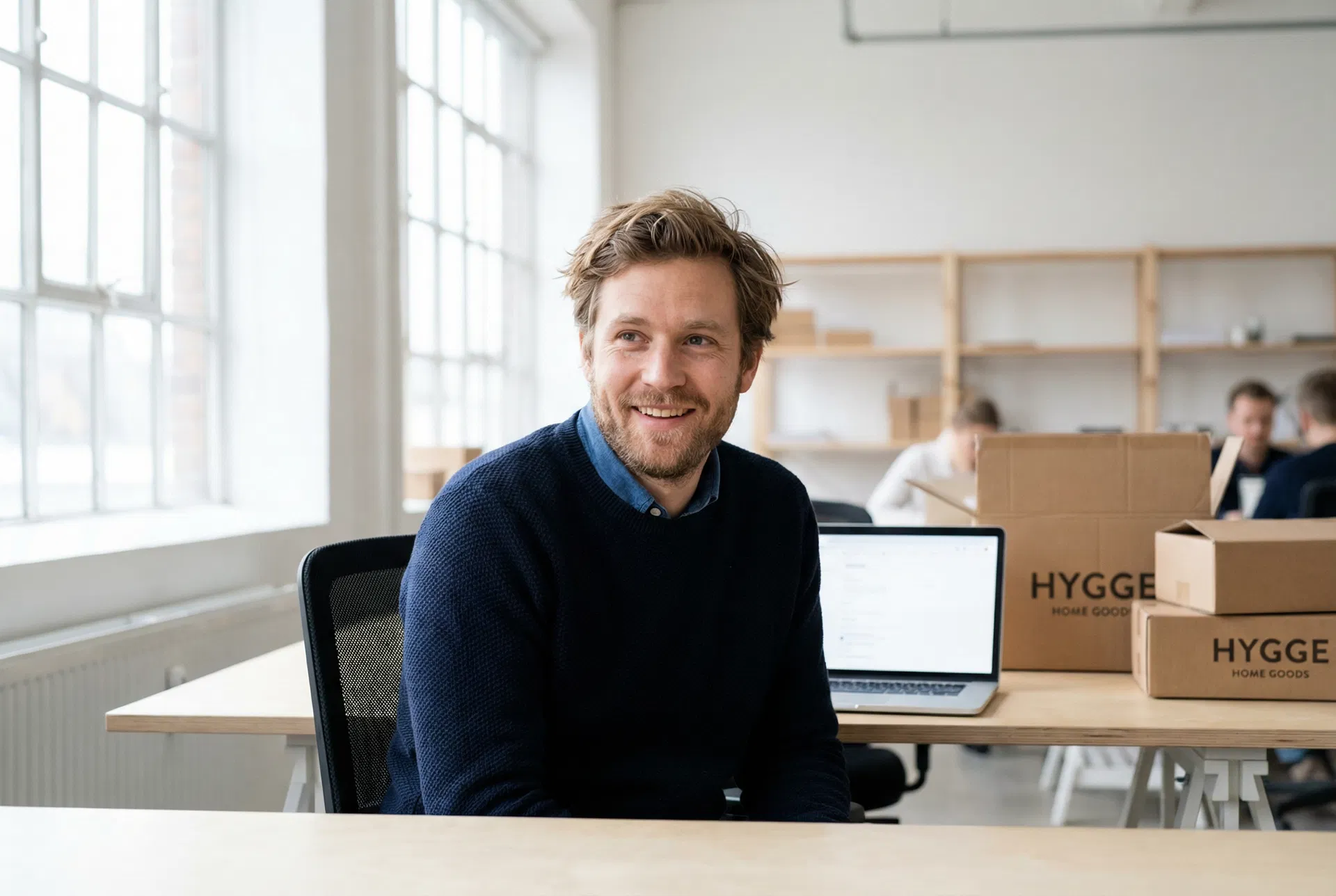 Dansk iværksætter i co-working space med laptop og forsendelseskasser