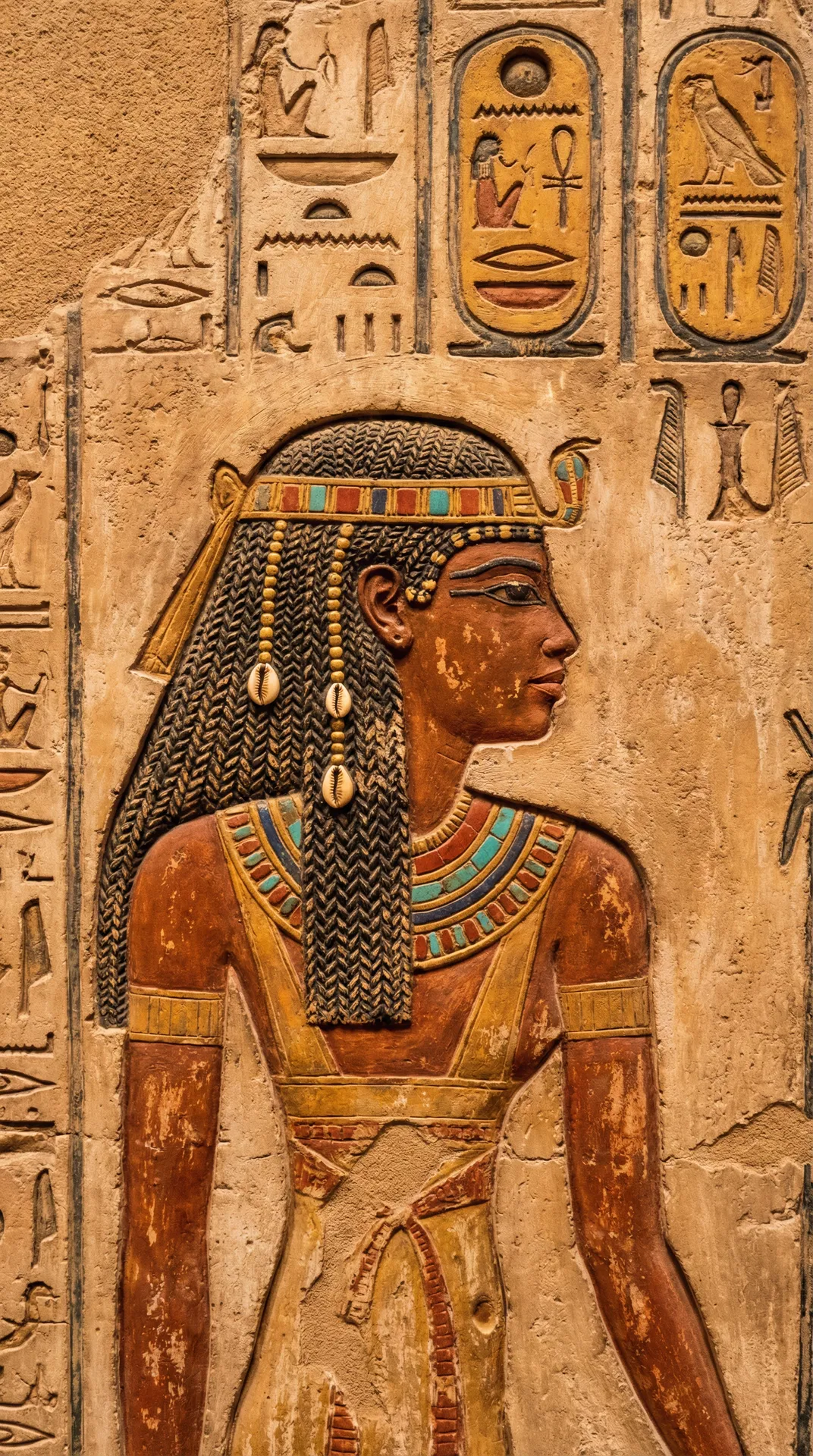 Ancient Egyptian hieroglyphic relief of a regal woman with braids adorned with gold beads and cowrie shells
