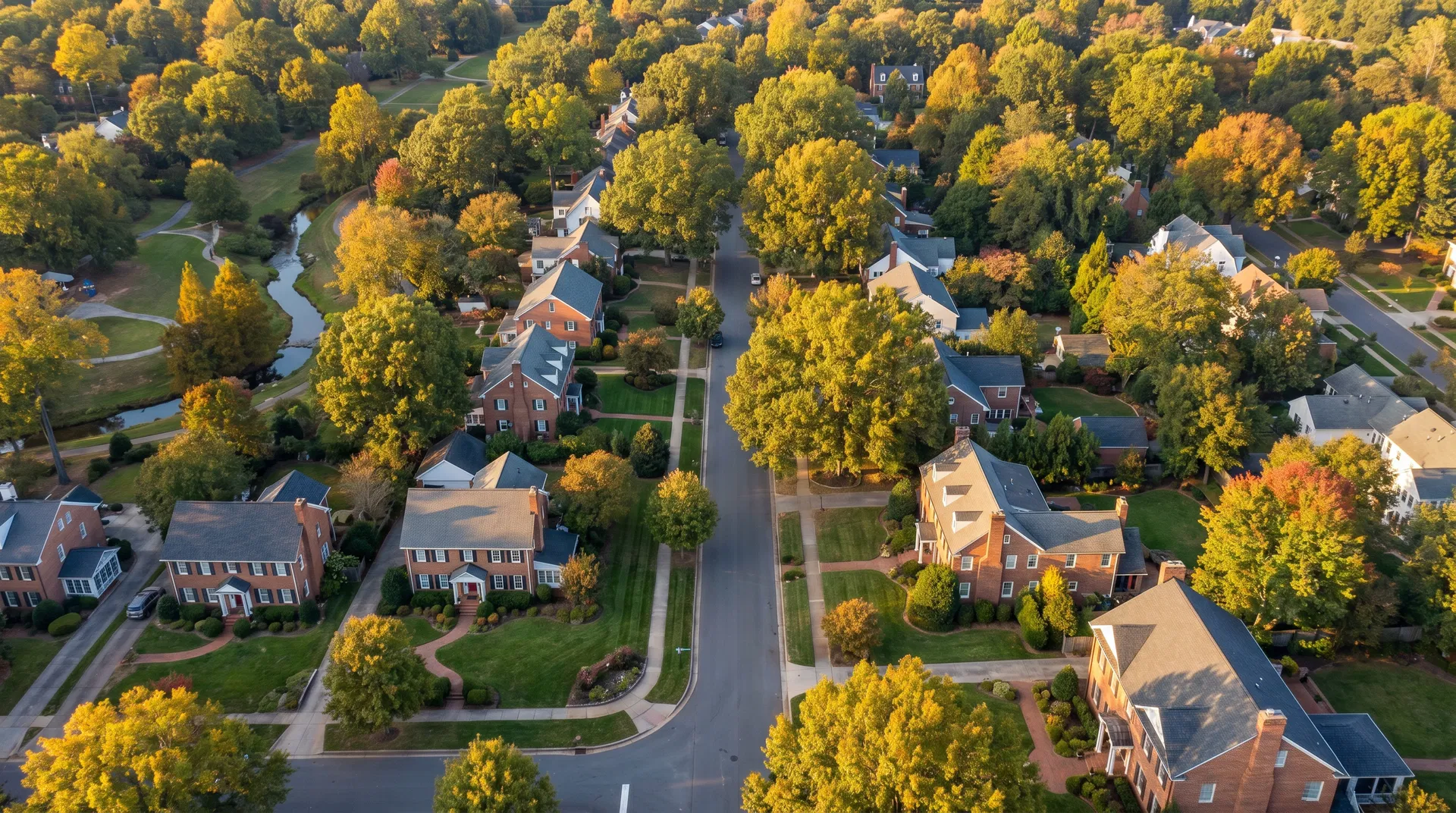 Aerial drone view of established Charlotte NC residential neighborhood with brick colonial homes, tree-lined streets, and manicured lawns at golden hour