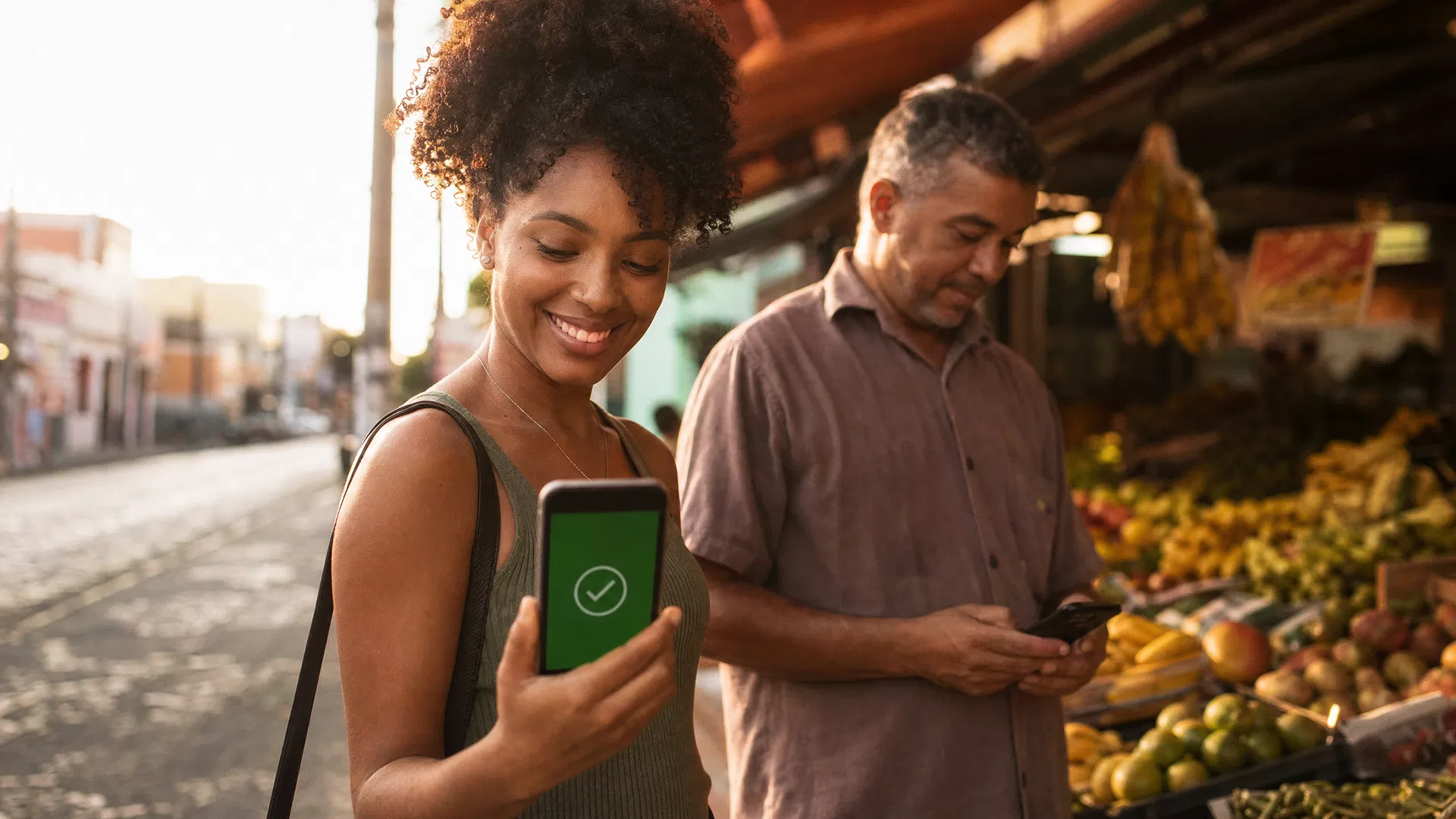 Mulher brasileira sorrindo ao usar PIX no celular em uma feira