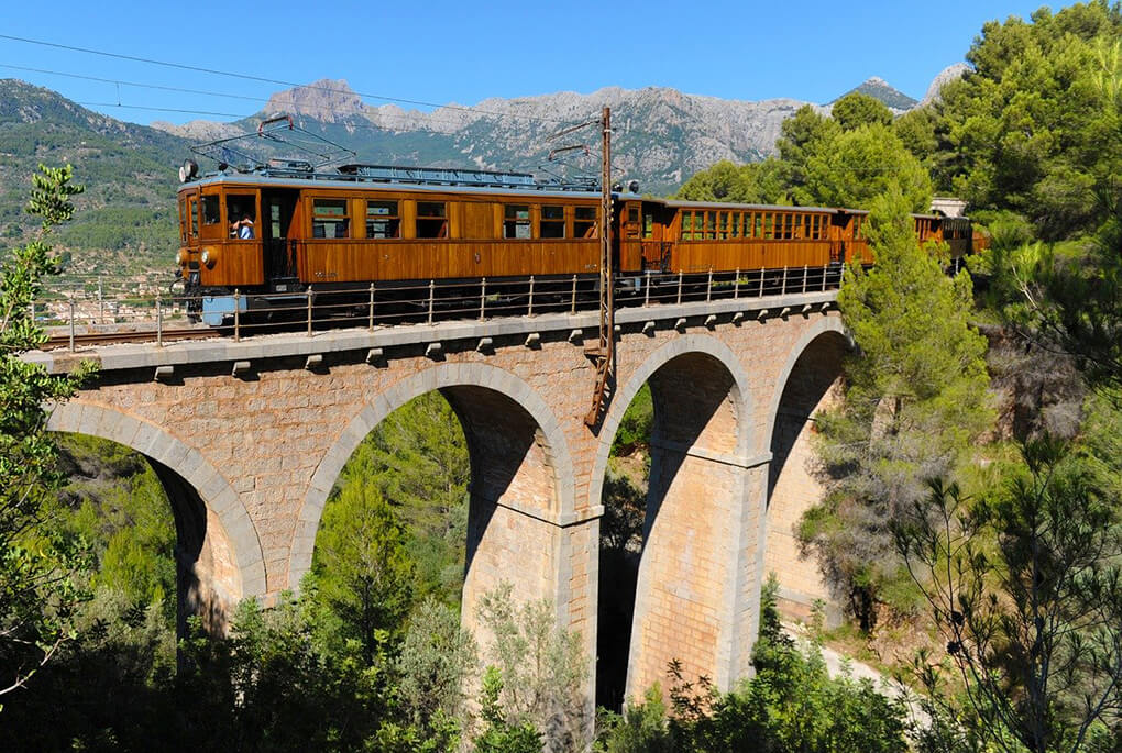 Historic Santa Gertrudis tram crossing a stone viaduct through a lush valley in Ibiza