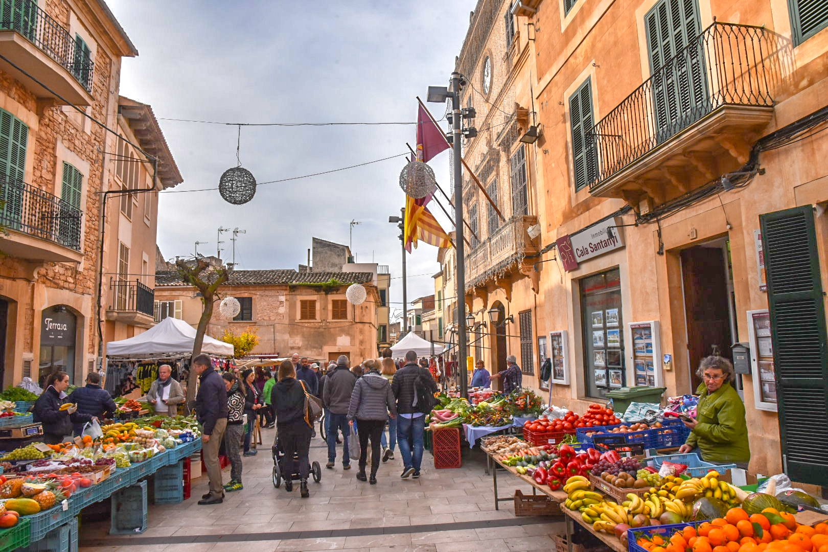 A bustling street market in Cala Jondal, Ibiza, with stalls under golden stone buildings