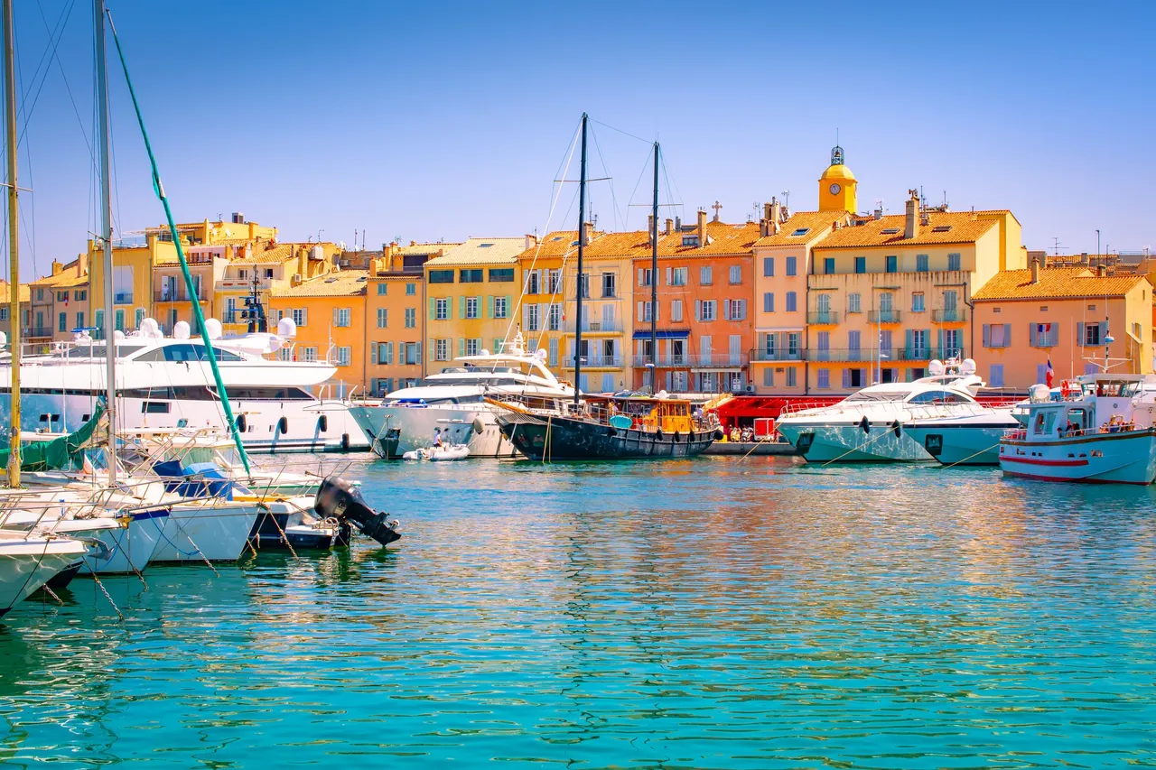 Luxury yachts and sailboats in Saint-Tropez marina before colourful historic buildings in France.