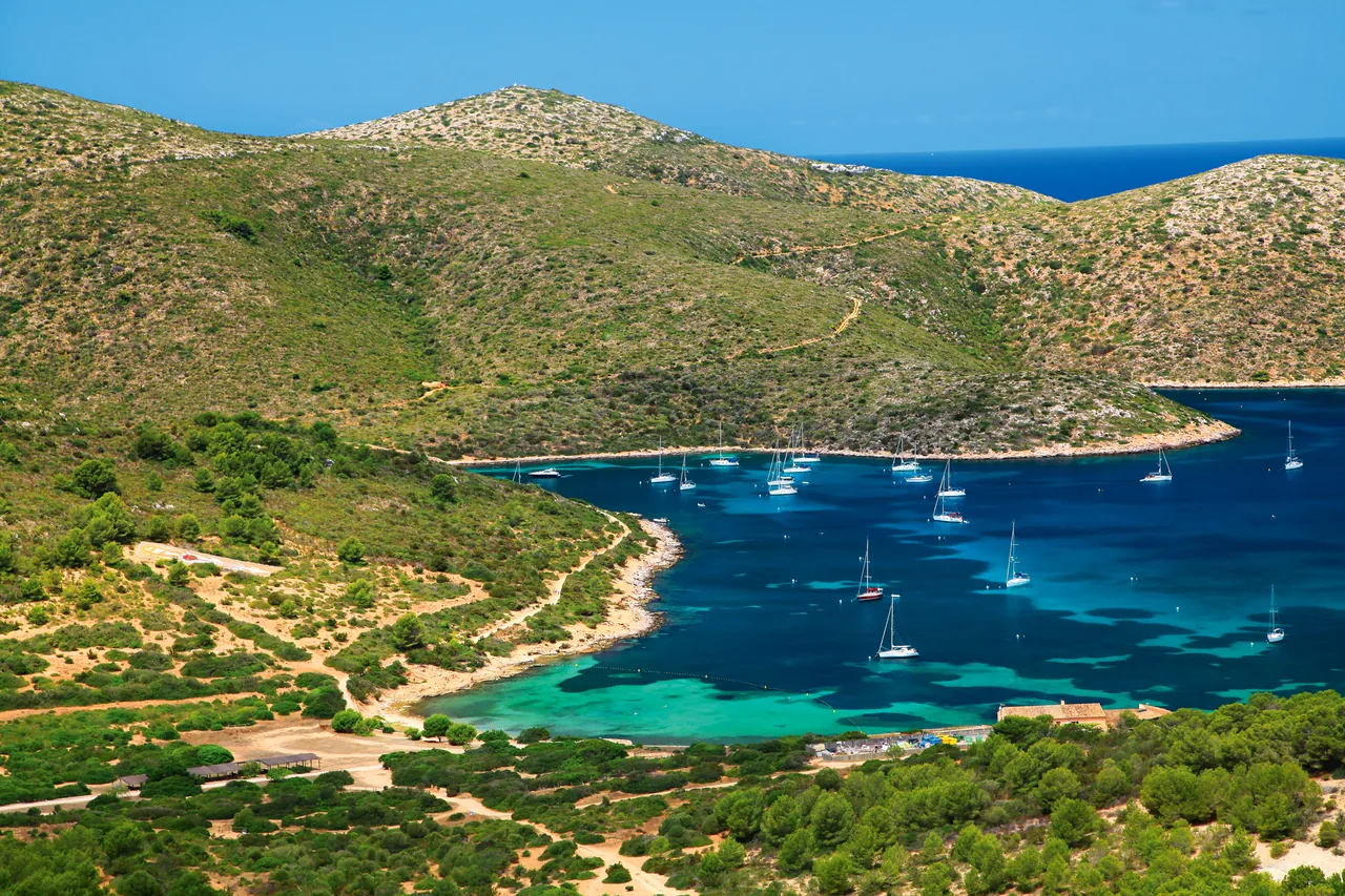 Aerial view of sailboats moored in the turquoise bay of Cabrera Archipelago Maritime-Terrestrial National Park, Spain.