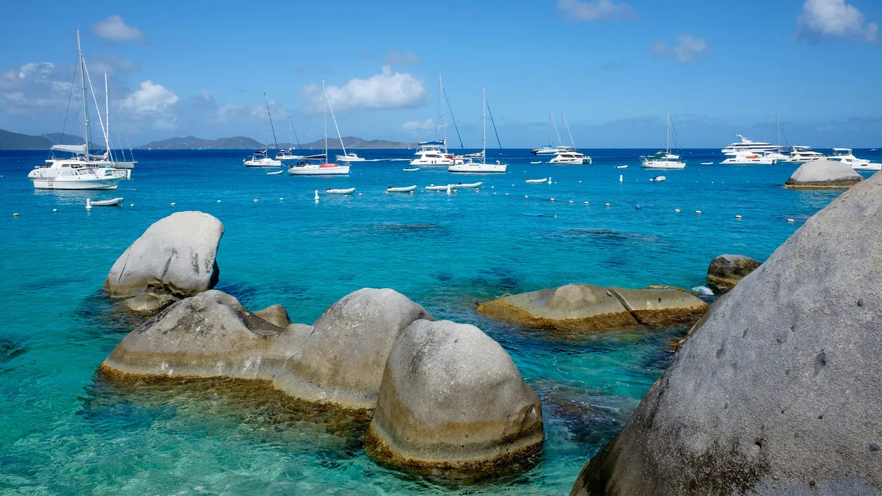 Granite boulders and yachts at The Baths, Virgin Gorda, BVI, beside a beach.