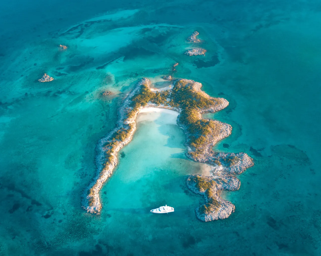 Aerial view of a white yacht anchored in a turquoise lagoon beside an unidentified tropical island.