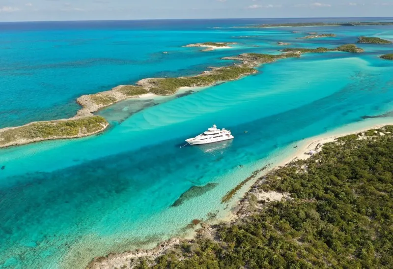 Aerial view of a white motor yacht in turquoise channels of the Exumas, Bahamas.