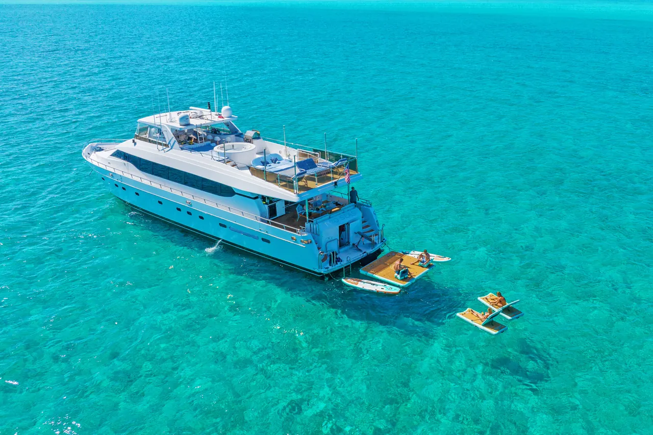 Aerial view of a white luxury yacht in tropical waters with guests on floating loungers.