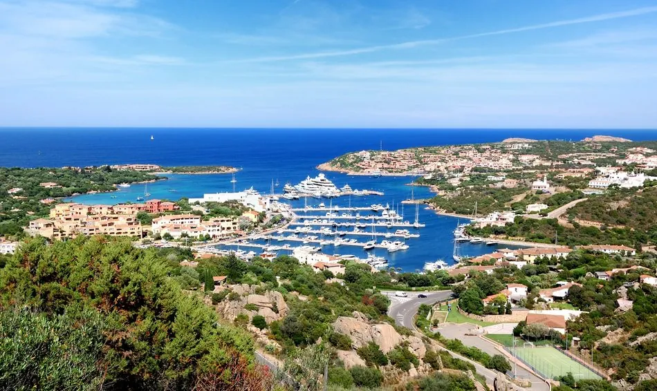 Aerial view of luxury yachts in Porto Cervo marina beside the coastal town in Sardinia, Italy.
