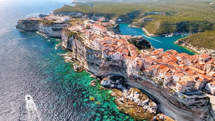 Aerial view of Bonifacio’s historic town on white limestone cliffs above turquoise water in Corsica.