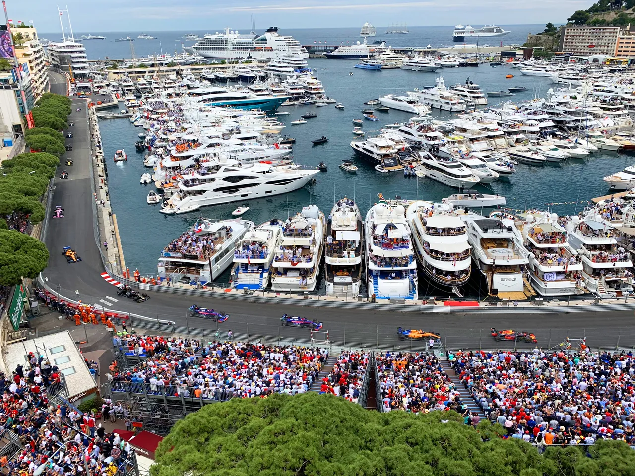 Aerial view of Formula 1 cars racing beside luxury yachts in Monaco, with crowds along the circuit