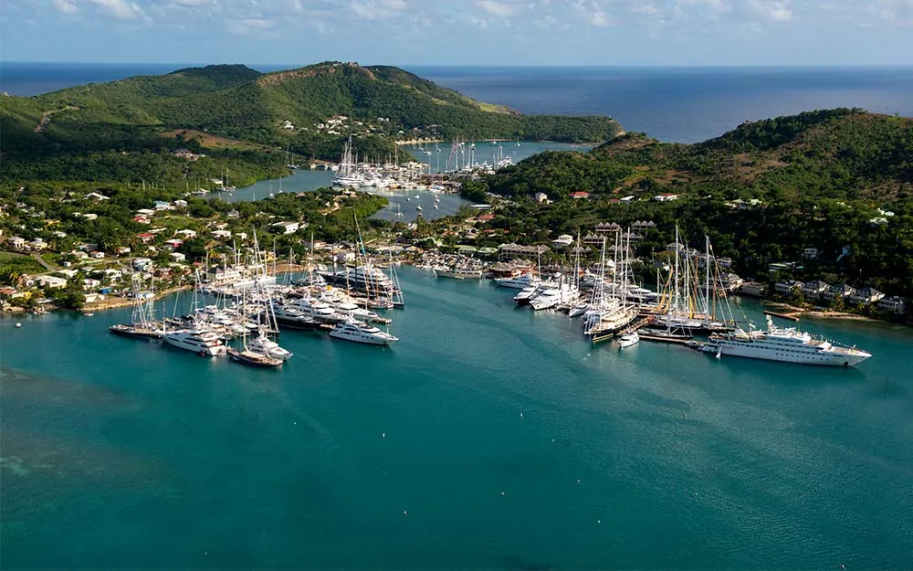 Aerial view of yachts and sailboats moored in English Harbour, Antigua, with green hills and turquoise water.