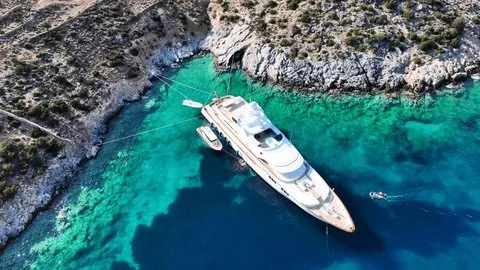 Aerial view of a luxury motor yacht anchored in a turquoise cove with tenders.
