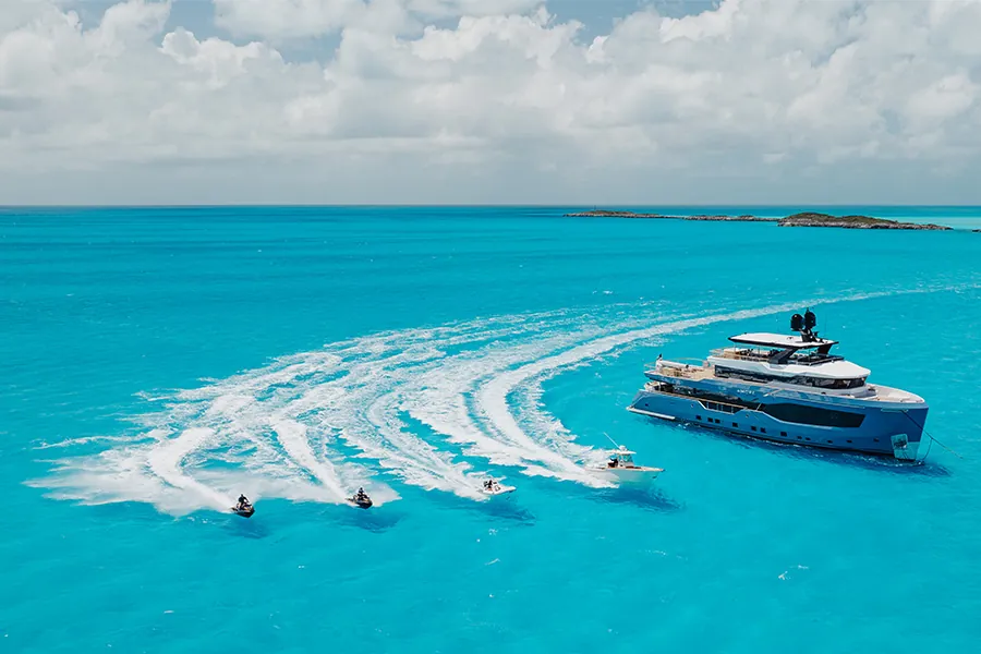 Aerial view of a blue motor yacht with a tender and jet skis in turquoise water.