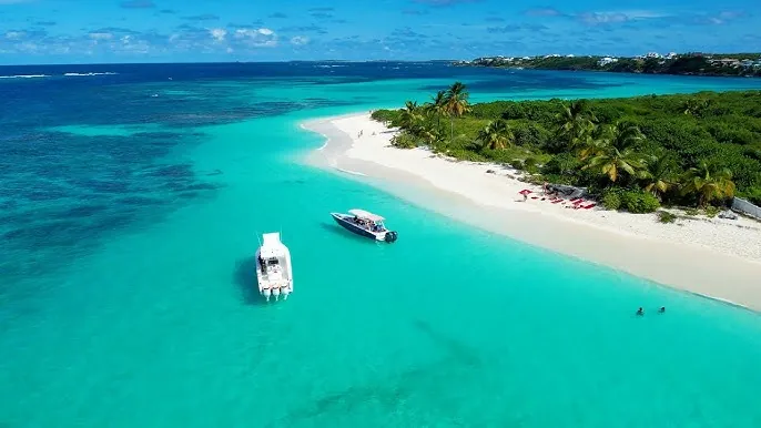 Aerial view of two motorboats off Shoal Bay East’s white sand point in Anguilla, with turquoise water and palm trees.