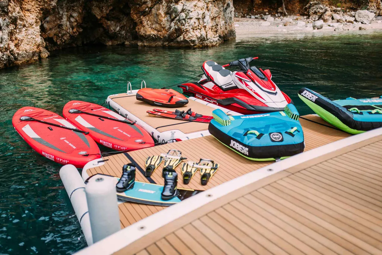 Jet ski and paddleboards ready on a yacht's swim platform in a quiet cove