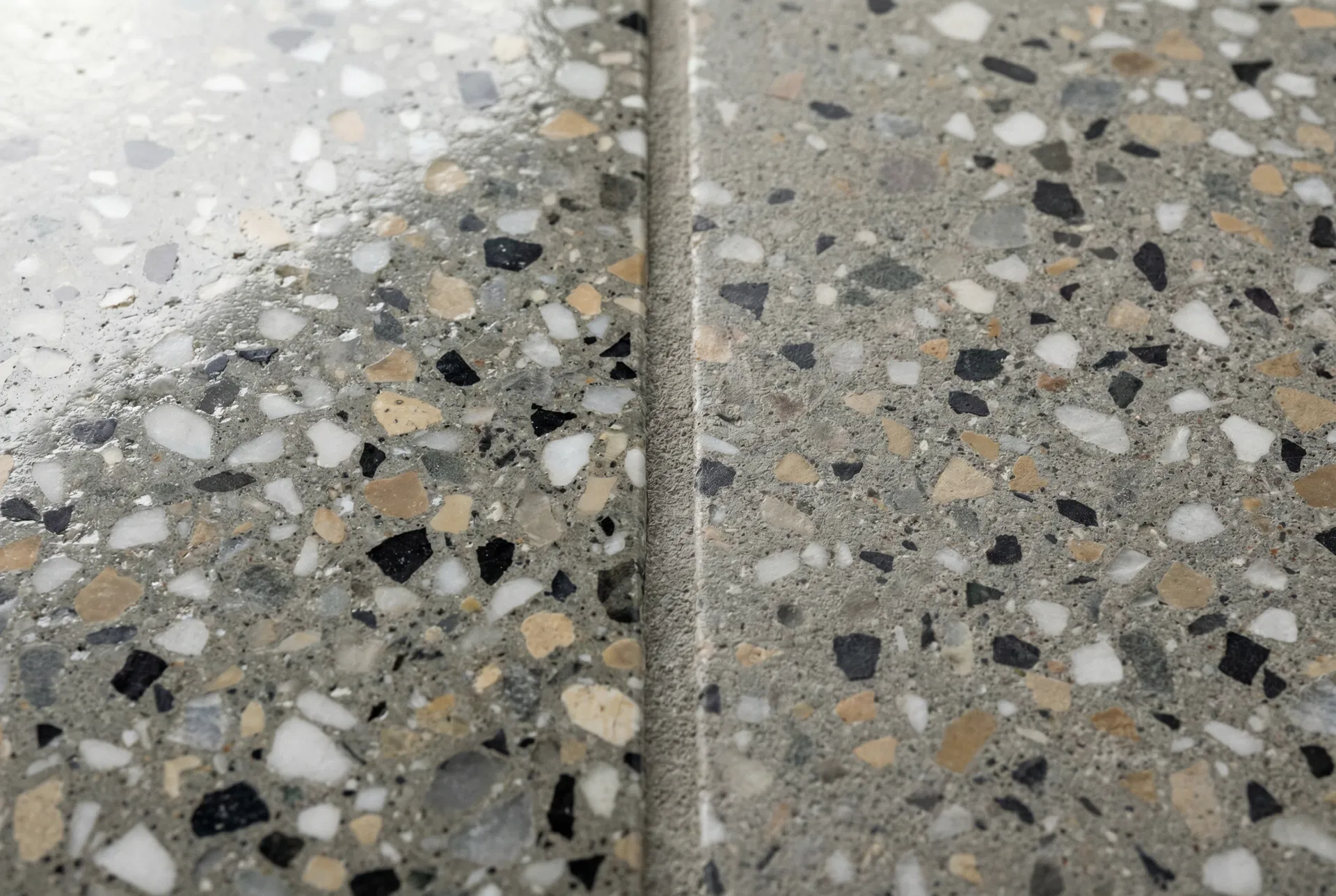 Nahaufnahme von Betonwerkstein-Platten mit typischer Sprenkelung und Zuschlagkörnern aus Marmorsplitt, Basalt und Quarzsand (KI-generiertes Illustrationsbild)