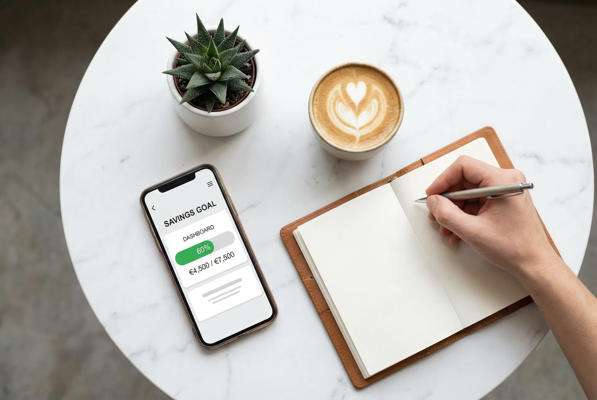 A phone showing a savings goal progress dashboard on a clean desk with coffee and a planner