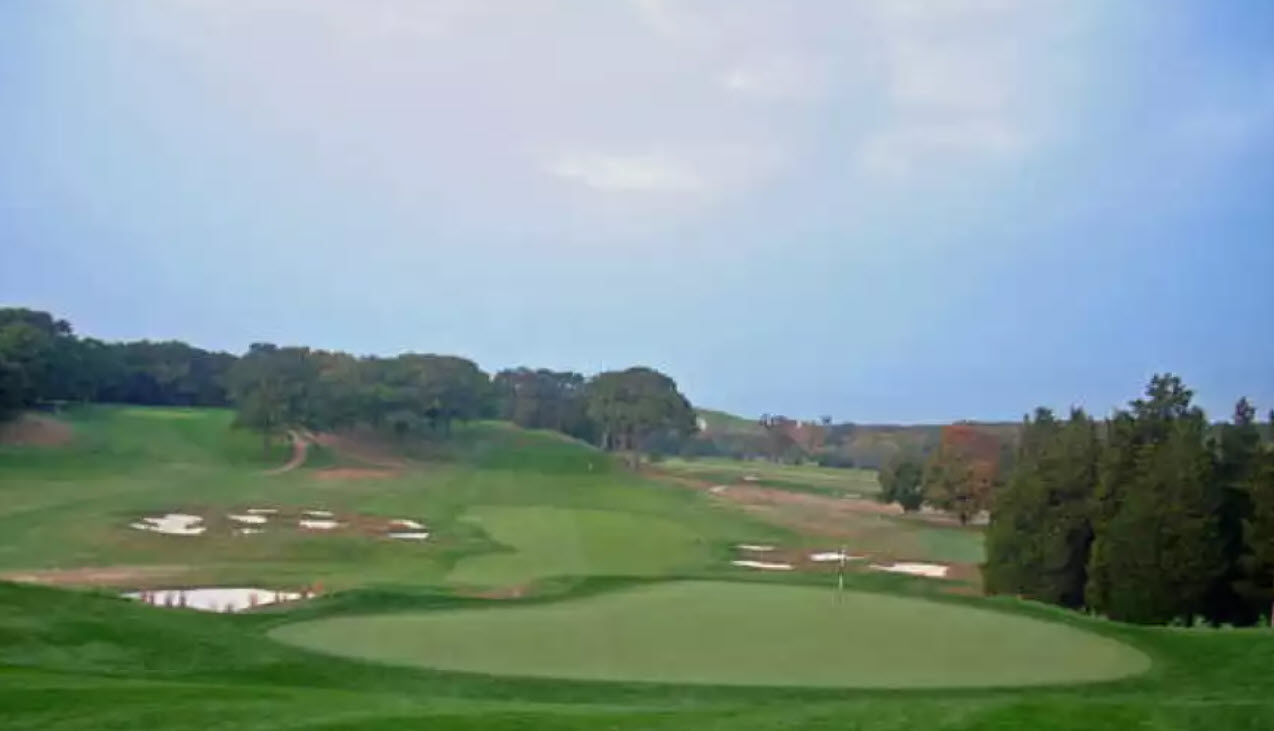 Aerial view of the Bethpage Black Course clubhouse and 18th green with golfers on the fairway