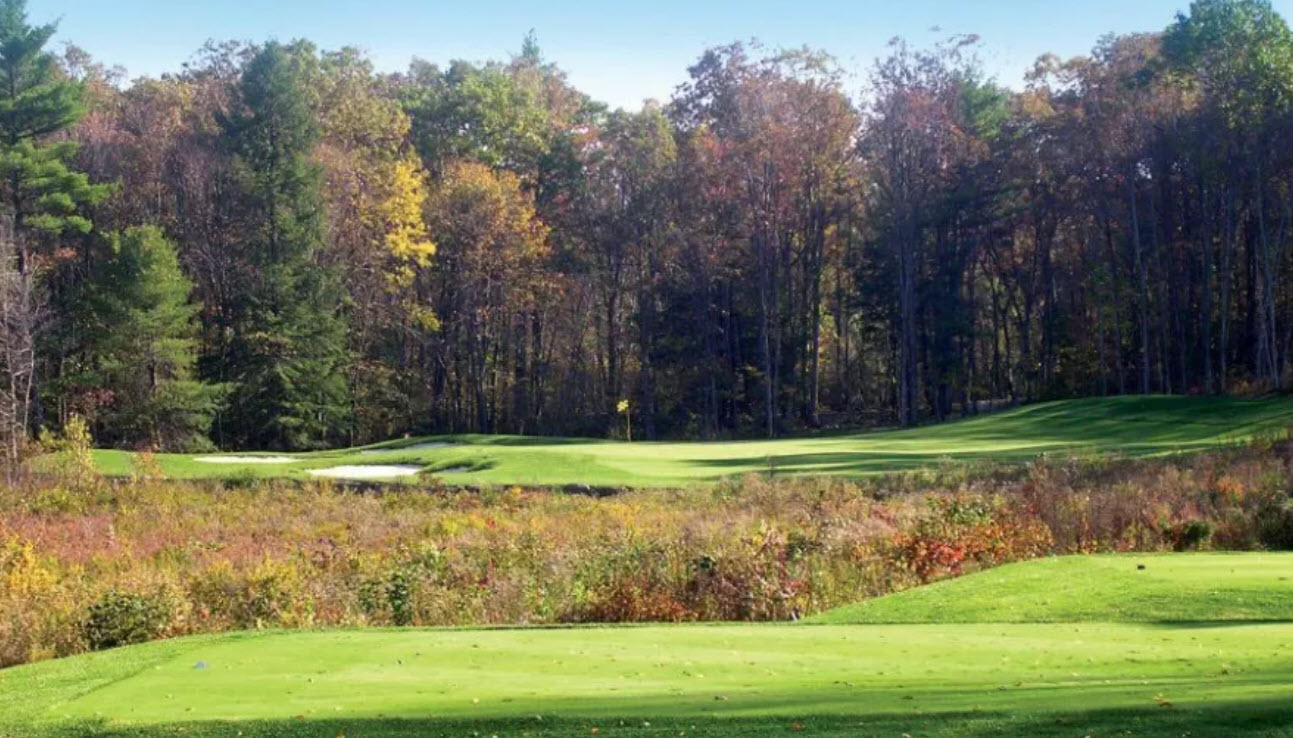 Panoramic view of a lush green golf course fairway at Blue Ridge Trail Golf Club with distant mountains under a blue sky.