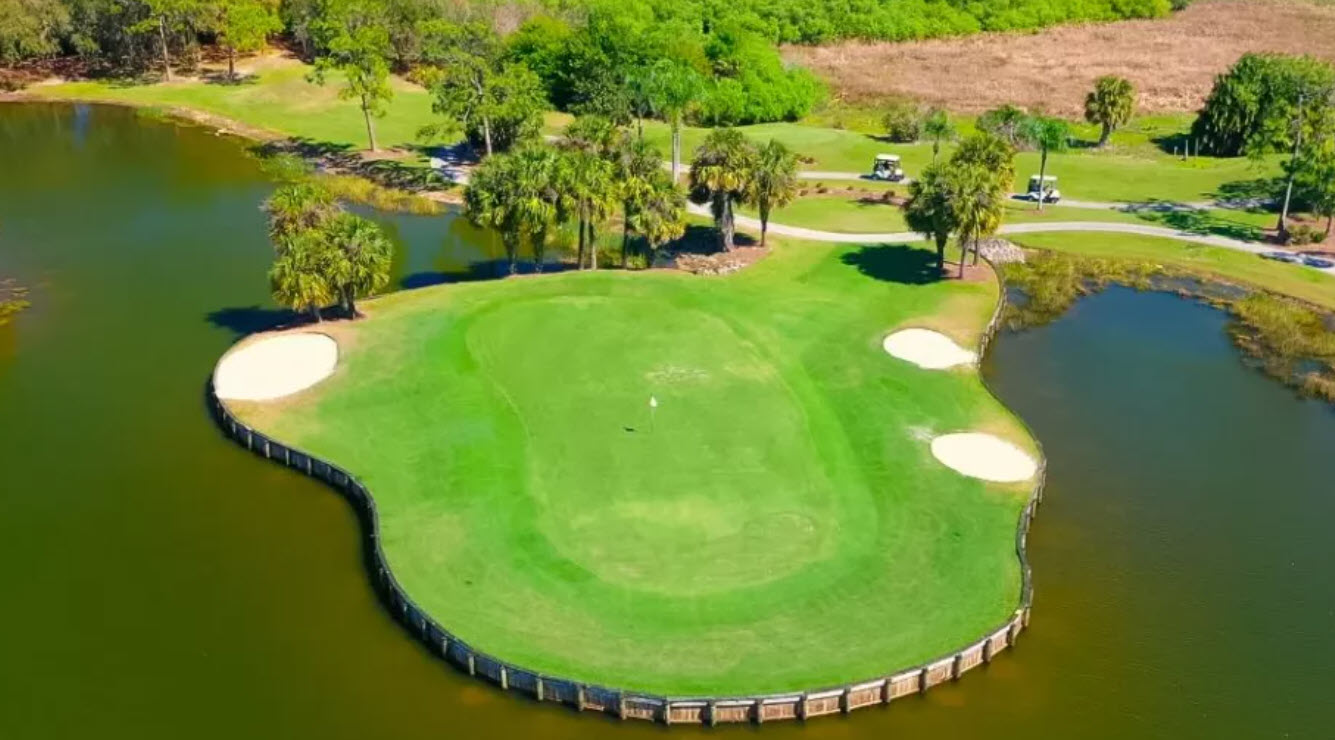 Scenic view of a lush green golf course fairway with a water hazard and palm trees under a blue sky at Herons Glen Golf & Country Club