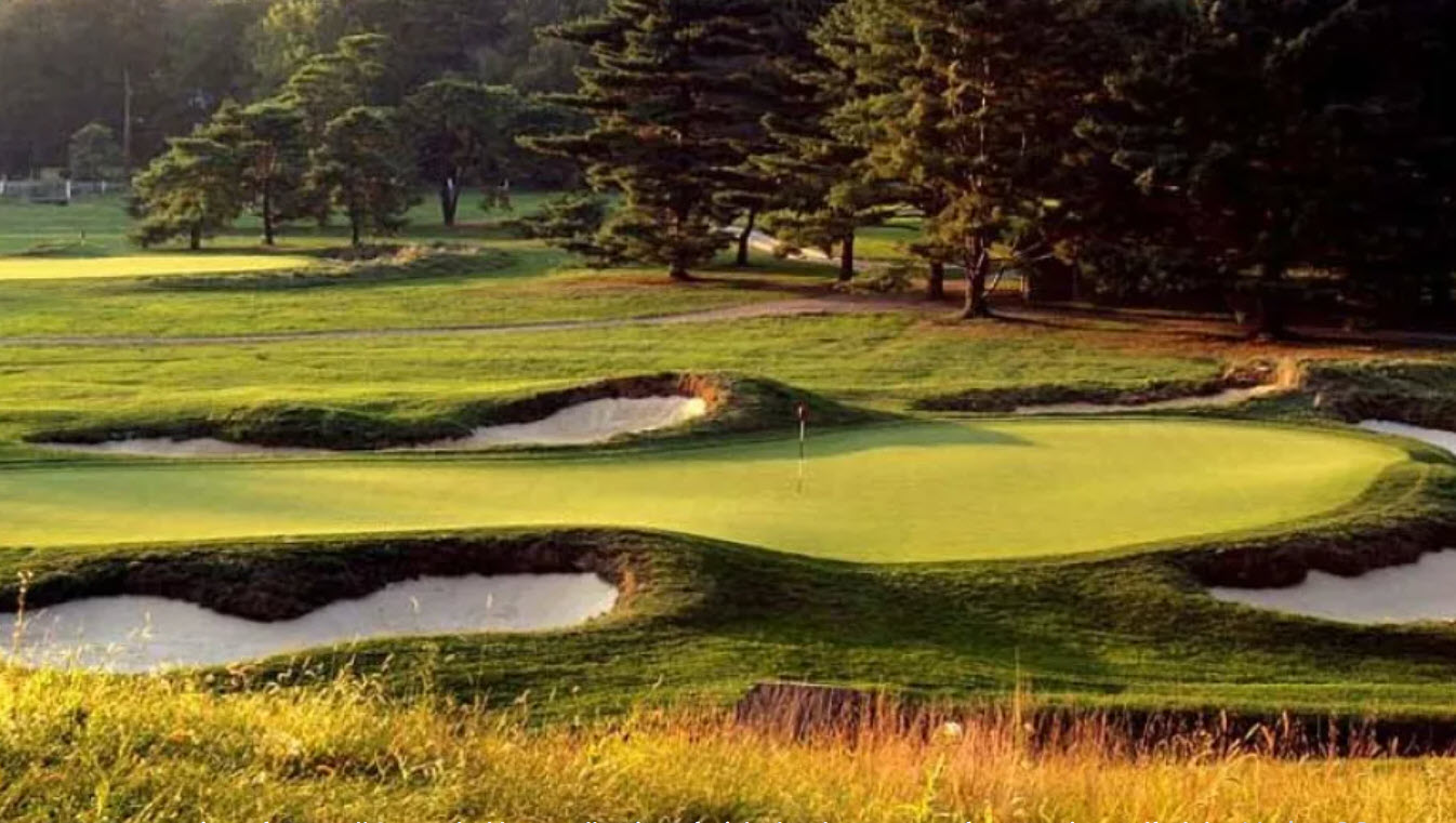Aerial view of Merion Golf Club East Course with iconic wicker basket flagsticks and lush green fairways under a clear sky.