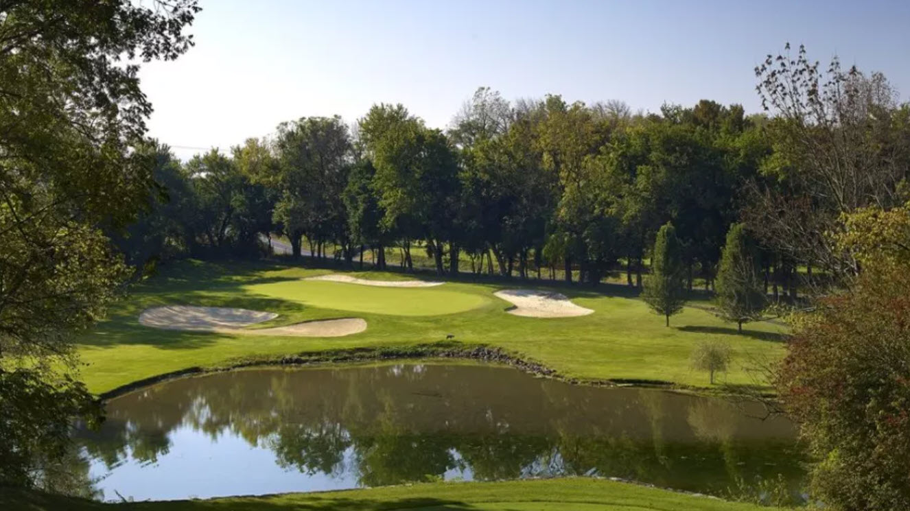 Scenic view of a green and fairway at Moselem Springs Golf Club with mature trees and blue sky