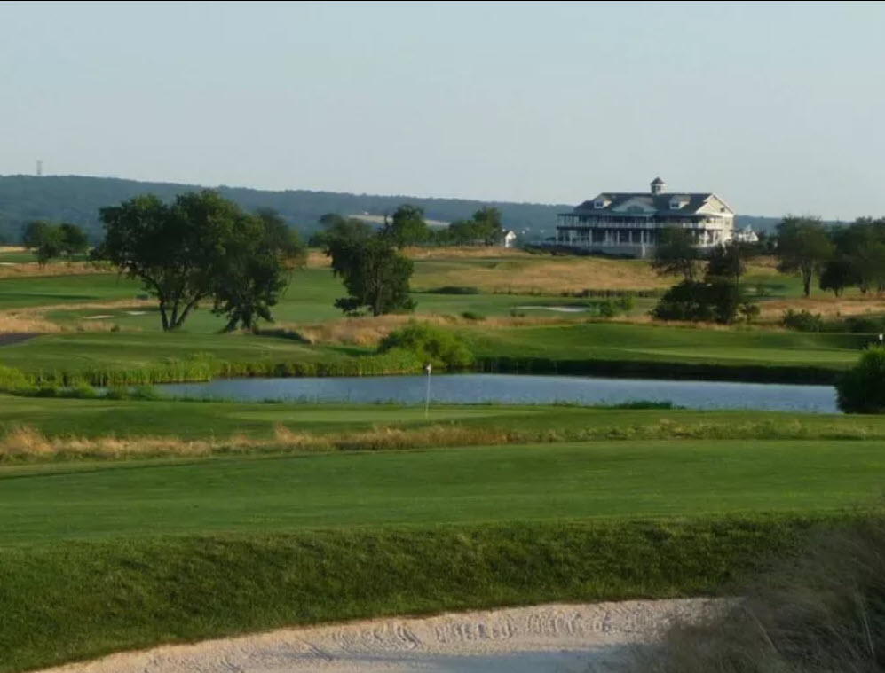 Panoramic view of Neshanic Valley Golf Course with lush fairways, greens, and distant trees under a clear sky.