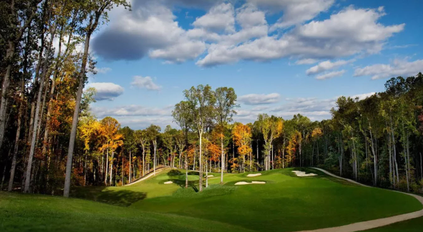 Scenic view of a golf hole at Potomac Shores Golf Club with a green, bunkers, and trees, under a clear sky.