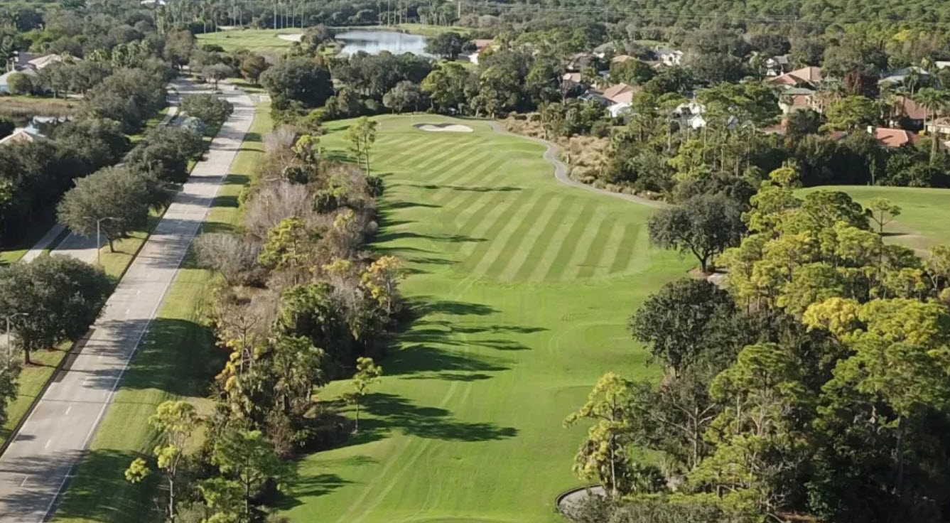 Scenic view of a lush green golf course fairway at Riverwood Golf Club with a water hazard and palm trees under a blue sky