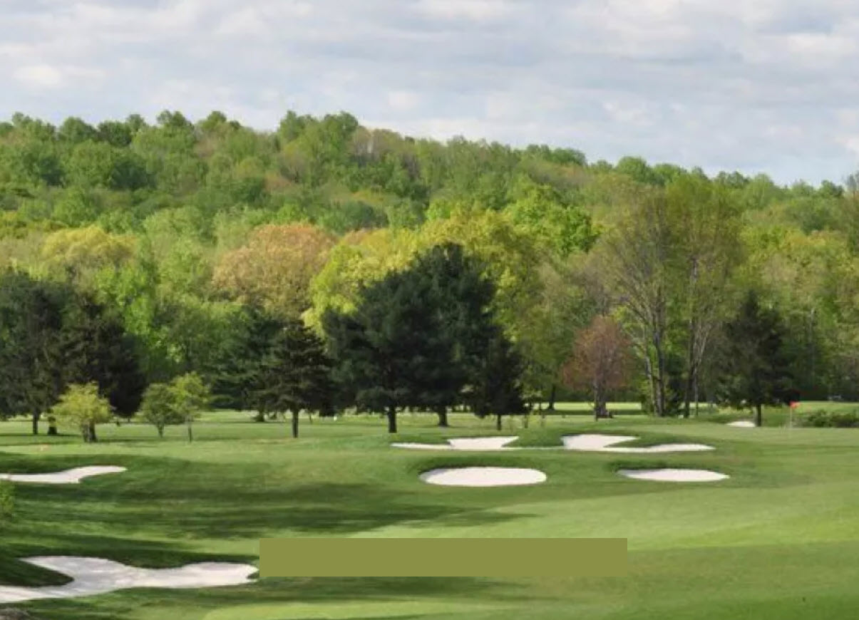 Overview of a green and fairway at Sunset Valley Golf Course with mature trees and blue skies