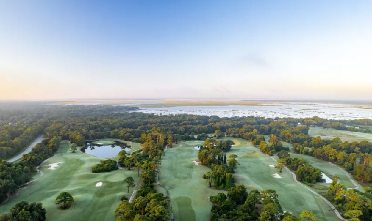 Panoramic view of a green at Amelia River Club with water hazards and marshland in the background under a blue sky.