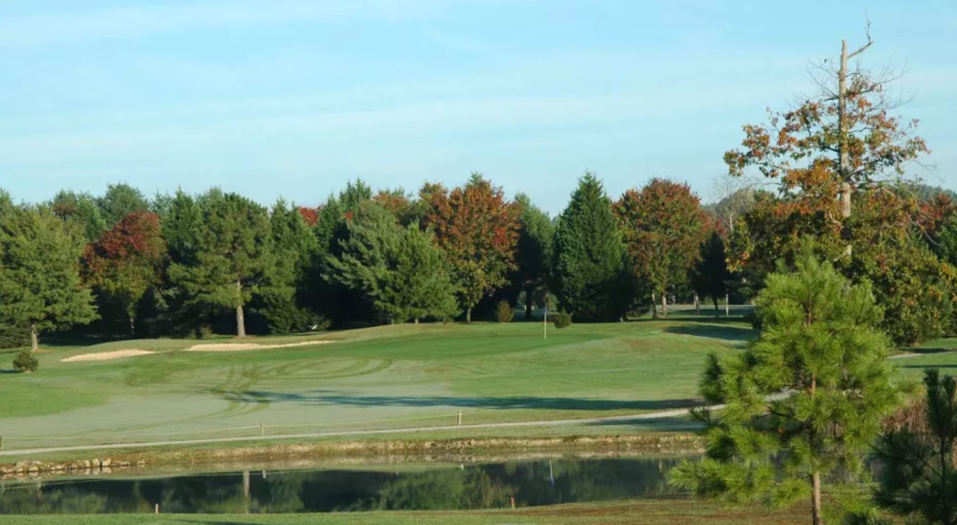 Scenic view of a green and fairway at The Hollows Golf Club with mature trees in the background