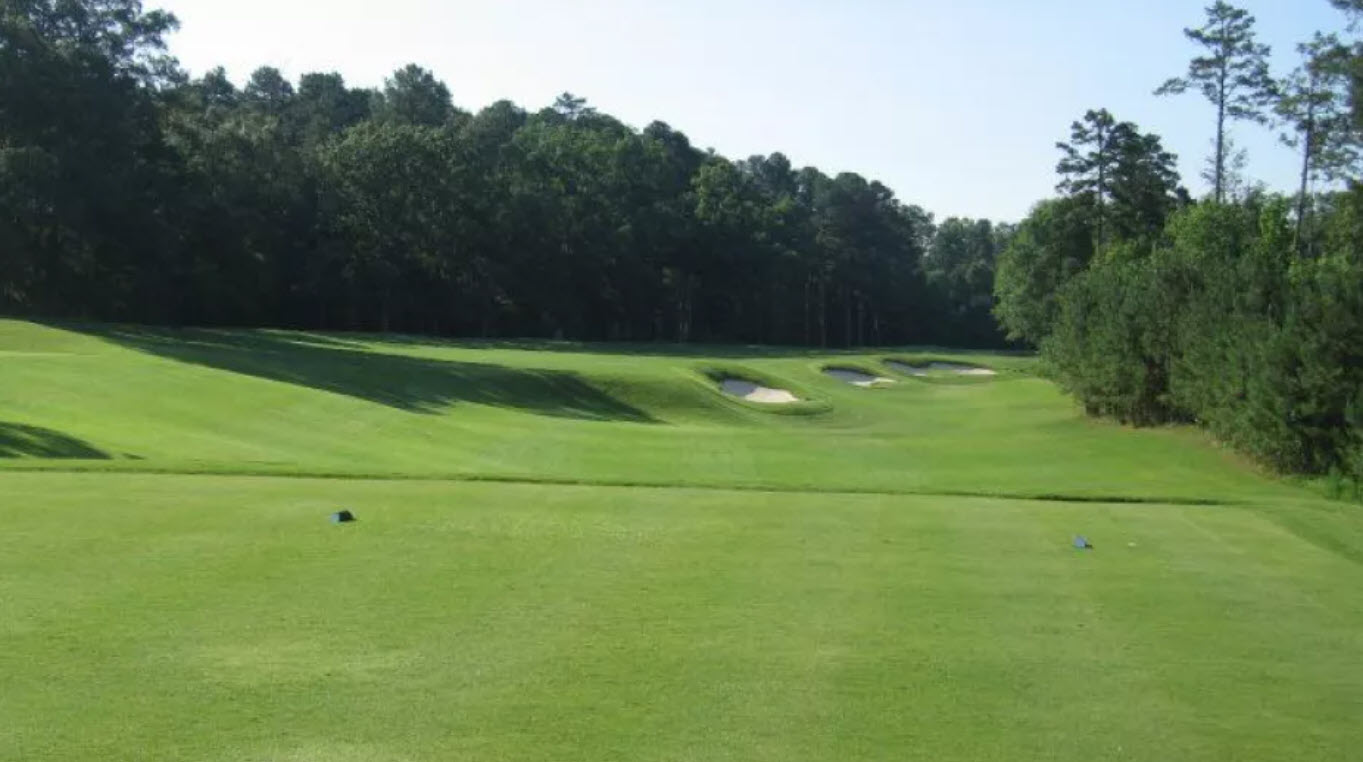 Panoramic view of a green and fairway at UNC Finley Golf Course with mature trees and blue sky.