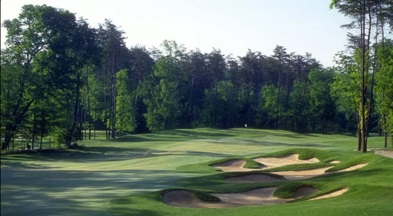 Scenic view of a lush green fairway at Westfields Golf Club with mature trees and bunkers under a blue sky.