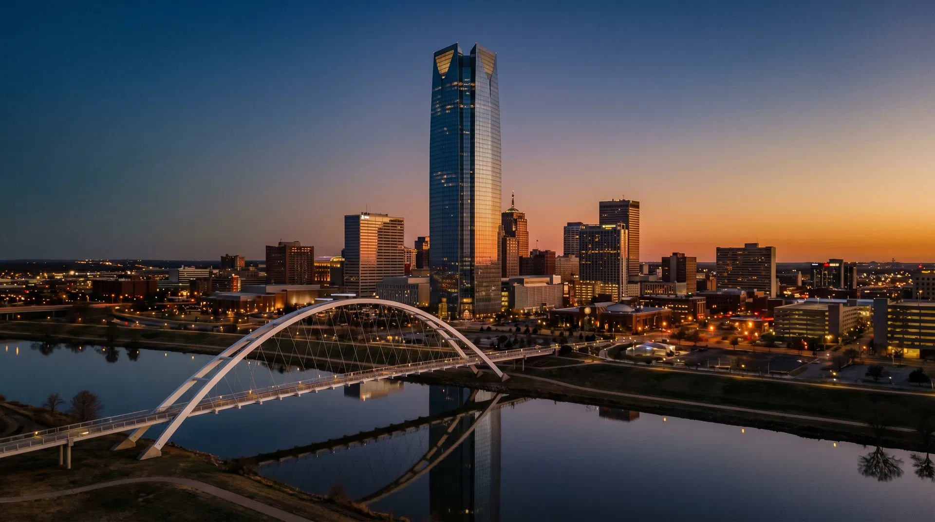 Oklahoma City skyline at dusk — Devon Tower and the Scissortail Park bridge reflected in the Oklahoma River at sunset