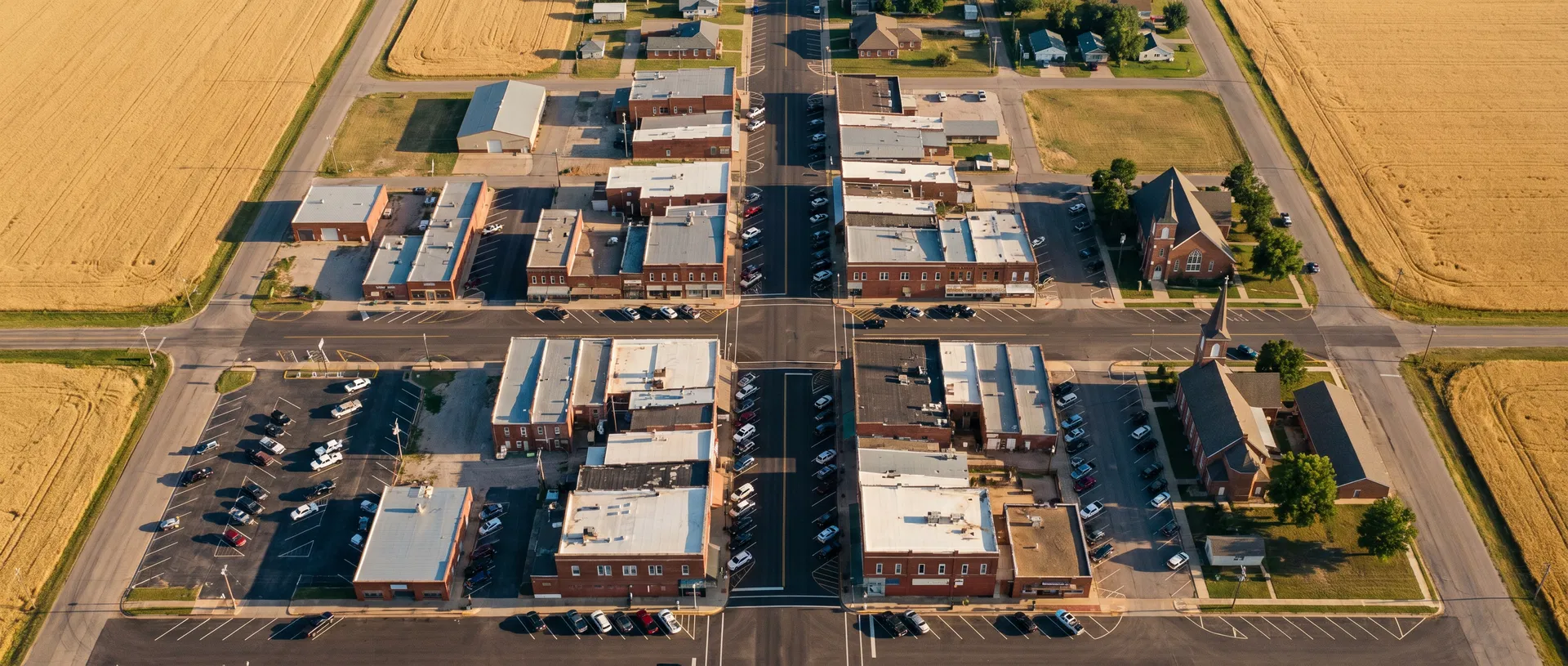 Aerial view of a classic American small town Main Street — brick buildings, wheat fields, and the grid pattern of heartland America