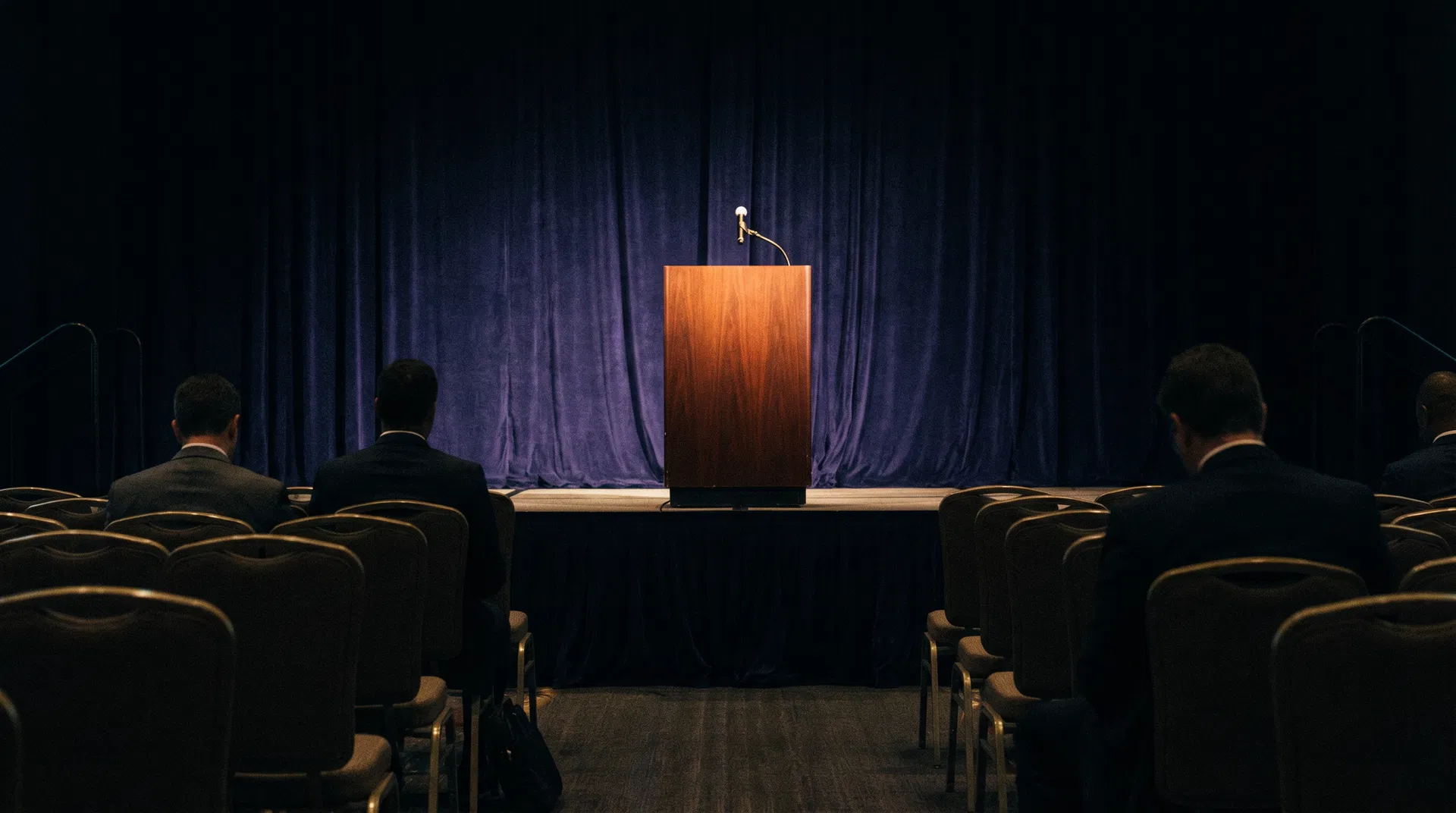 Professional conference stage with a podium and warm spotlights — intimate keynote setting for serious professionals