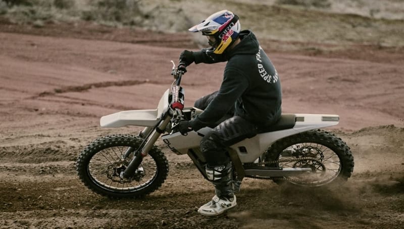 A motorcyclist wearing a helmet and protective gear rides a motorbike on a dusty track, making a sharp turn with dirt flying around.