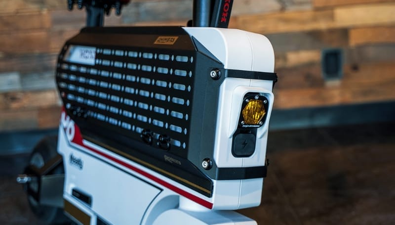 Close-up of the customized yellow rear brake light and side panel of a compact, foldable electric scooter, reminiscent of the iconic Honda Motocompacto, against a wooden background.