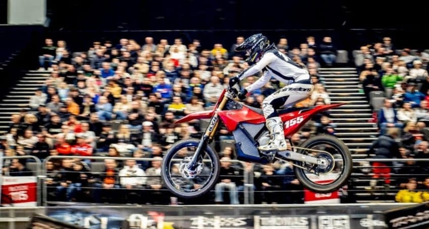 A motocross rider performing a jump during an indoor event in front of an audience.