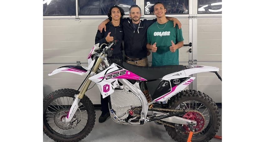 Three individuals posing with a thumbs-up gesture in front of a revolutionary Olivier S222 electric bike in a garage setting.