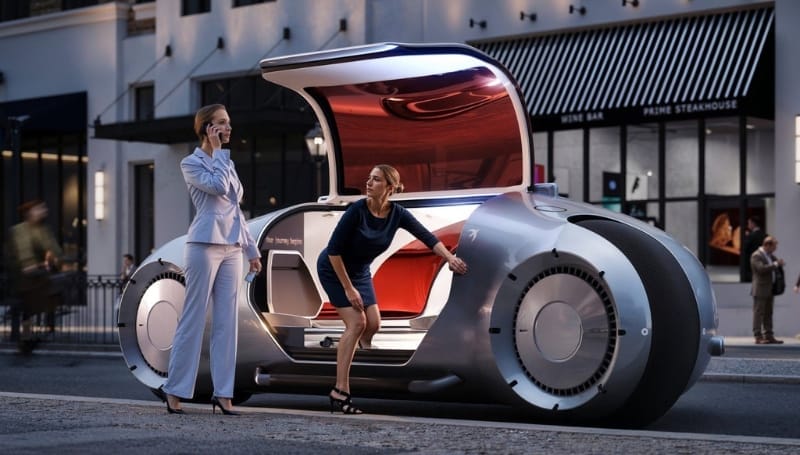 A futuristic car with large wheels and gull-wing doors is parked on a city street. Two women are interacting with the car; one on the phone and the other entering the vehicle.