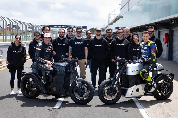 A group of people standing next to a group of Savic Motorcycles.
