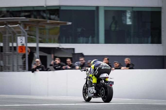 A person riding a motorcycle in front of a crowd, showcasing the thrill of high-speed tests with a C-Series Triumph or Savic motorcycle.