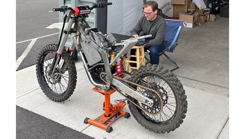 A man works on the Model-1 Prototype Motorbike elevated on a stand in a garage, using tools and focusing intently on the motorcycle.