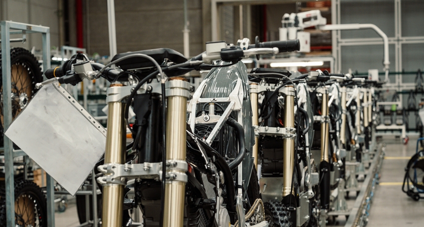 A row of partially assembled motorcycles in a factory setting, showing exposed frames and components with no body panels yet attached.