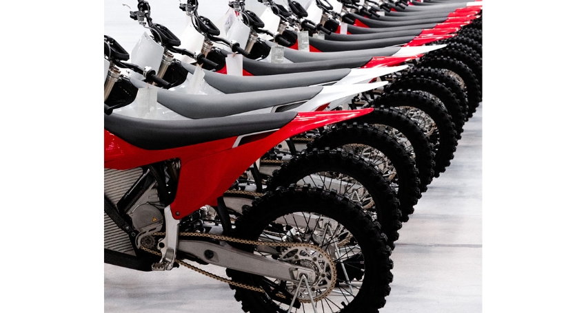 A row of red and white dirt bikes is lined up in a neat, organized fashion on a smooth, white floor.