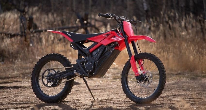 A red dirt bike sits on a dirt field.